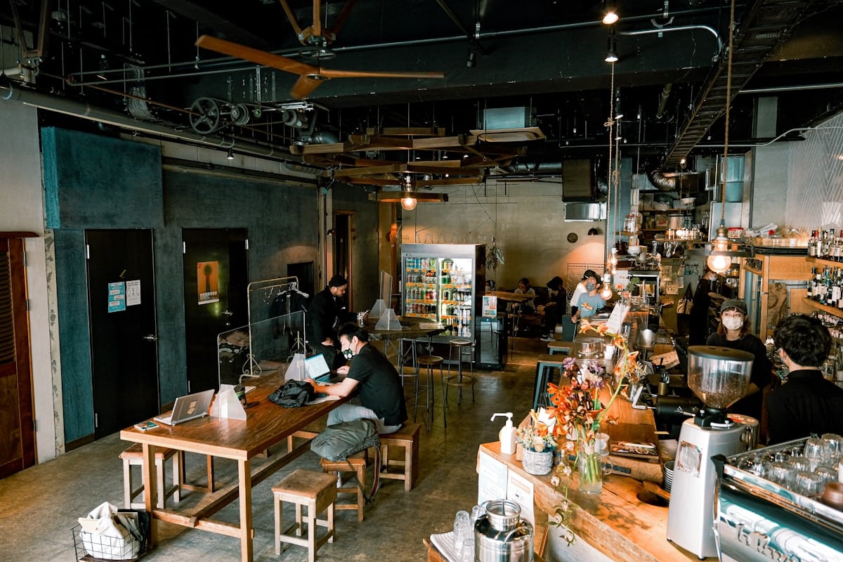 Café industriel avec des tables en bois, des clients et du matériel de cuisine.