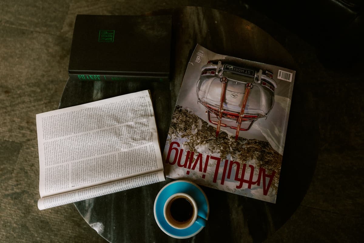 Un ordinateur portable, un magazine, un journal et un café sur une table.