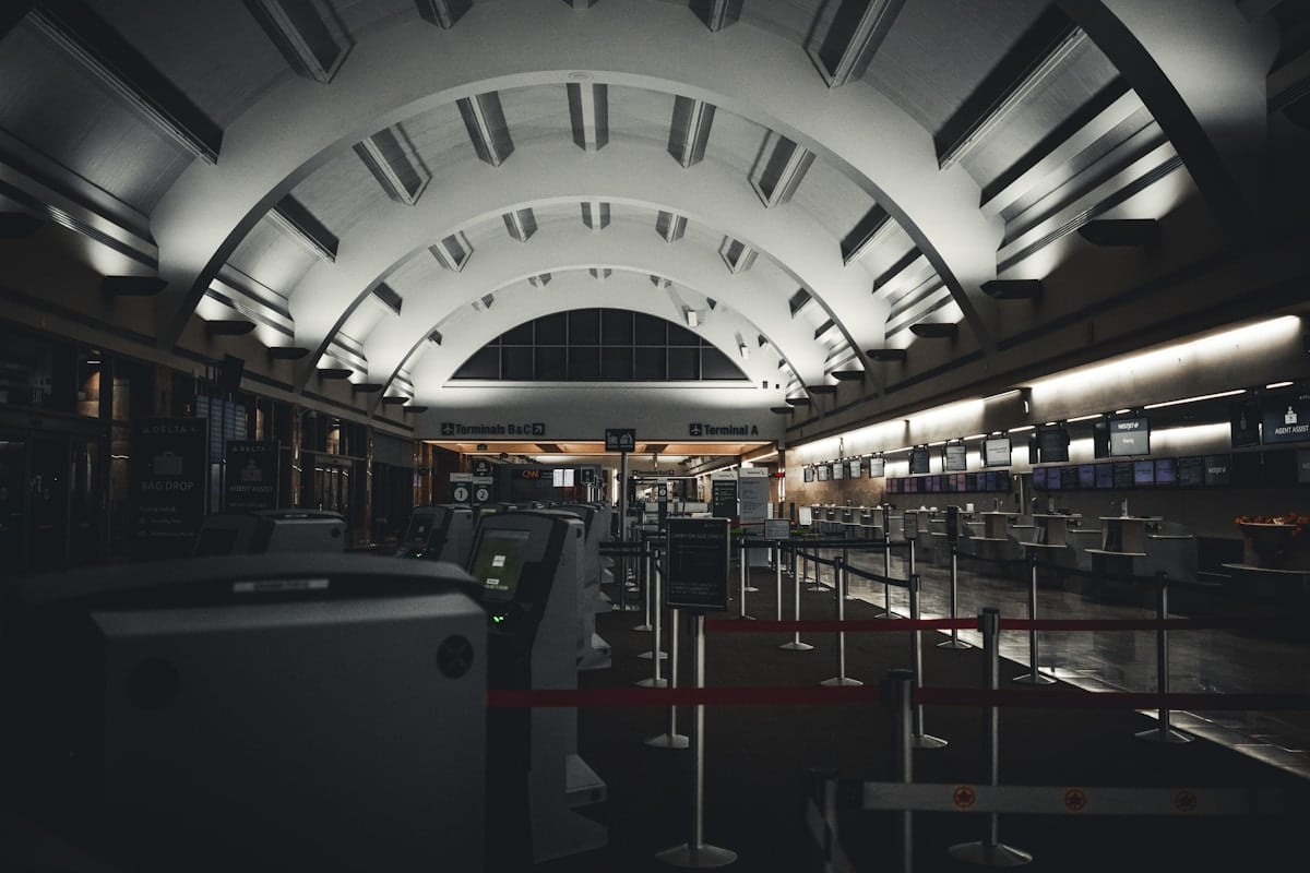 Vaste hall d'aéroport désert, avec des arches élégantes et des équipements de sécurité.