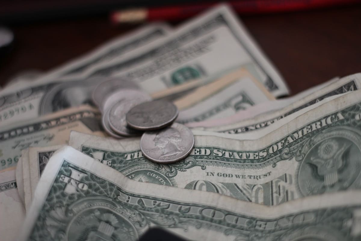 Billets de dollars américains et pièces de monnaie sur une surface sombre.