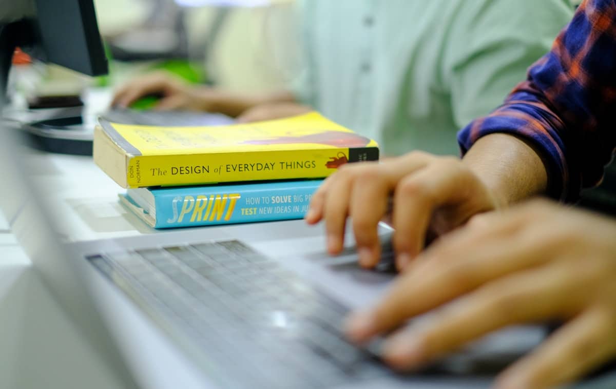 Mains d'une personne travaillant sur un ordinateur avec des livres sur la conception.