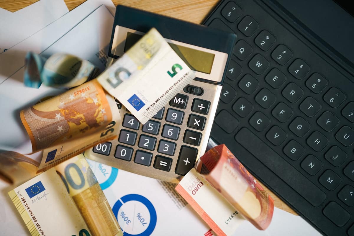 Calculatrice, billets en euros, documents financiers, stylo sur un bureau en bois.