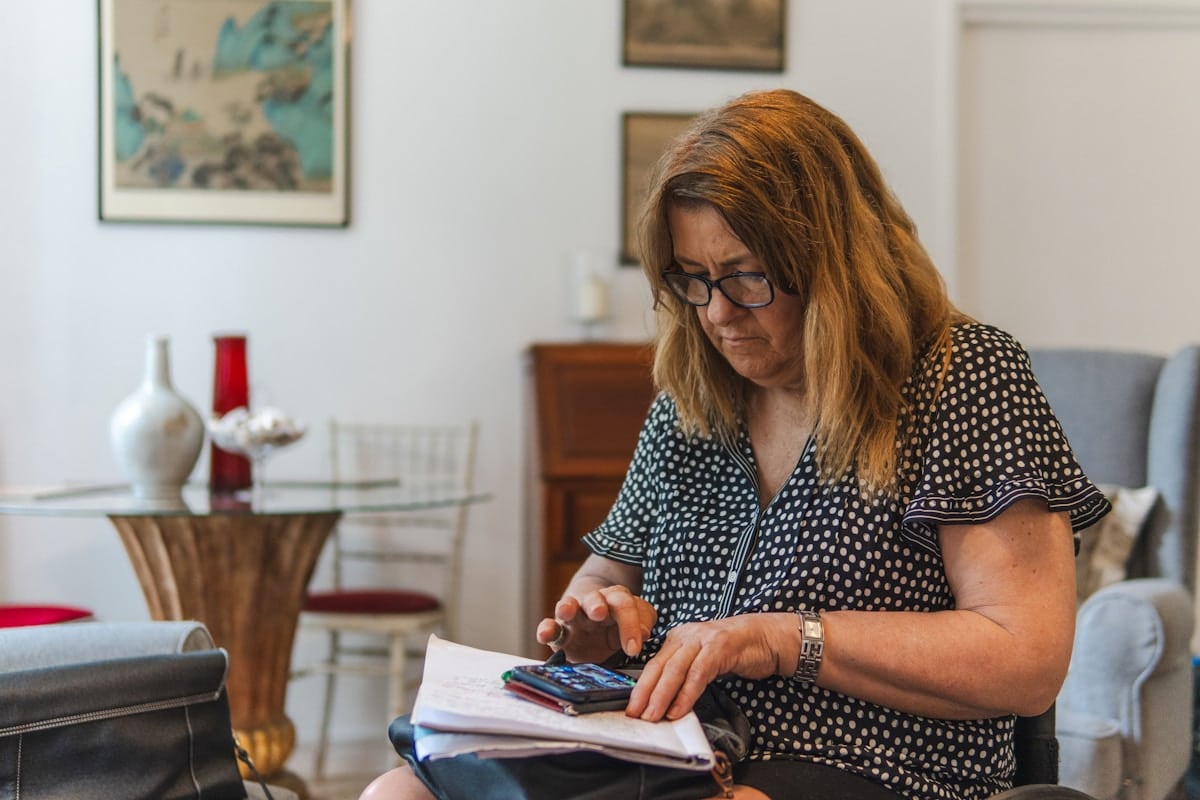 Femme assise dans un intérieur, utilisant une calculatrice et des documents.