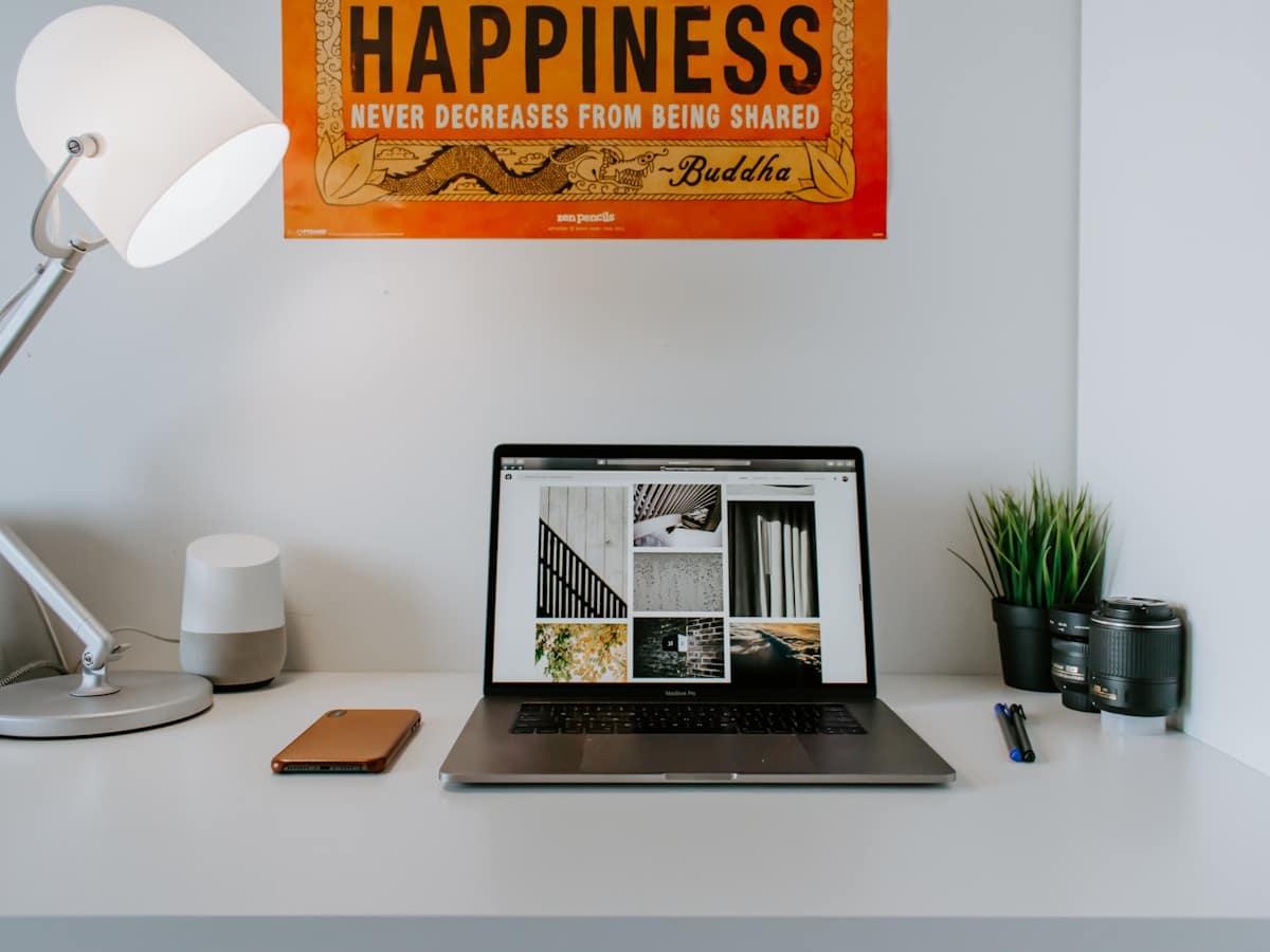 Bureau de travail avec ordinateur portable, lampe, plante et affiche "Happiness never decreases from being shared".