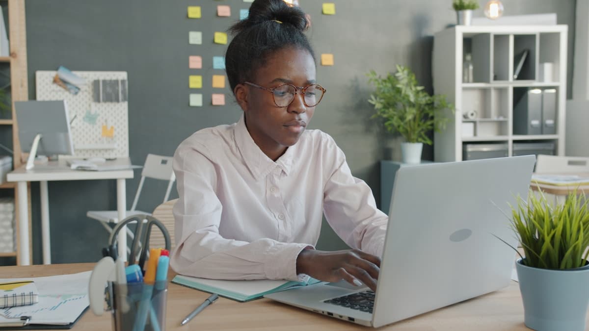 Femme afro-américaine concentrée, travaillant sur un ordinateur portable dans un bureau.