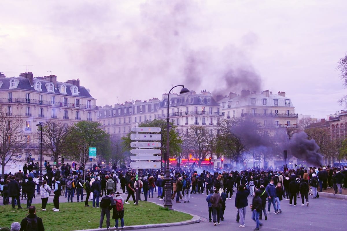 Foule manifestant dans un quartier parisien avec bâtiments historiques.