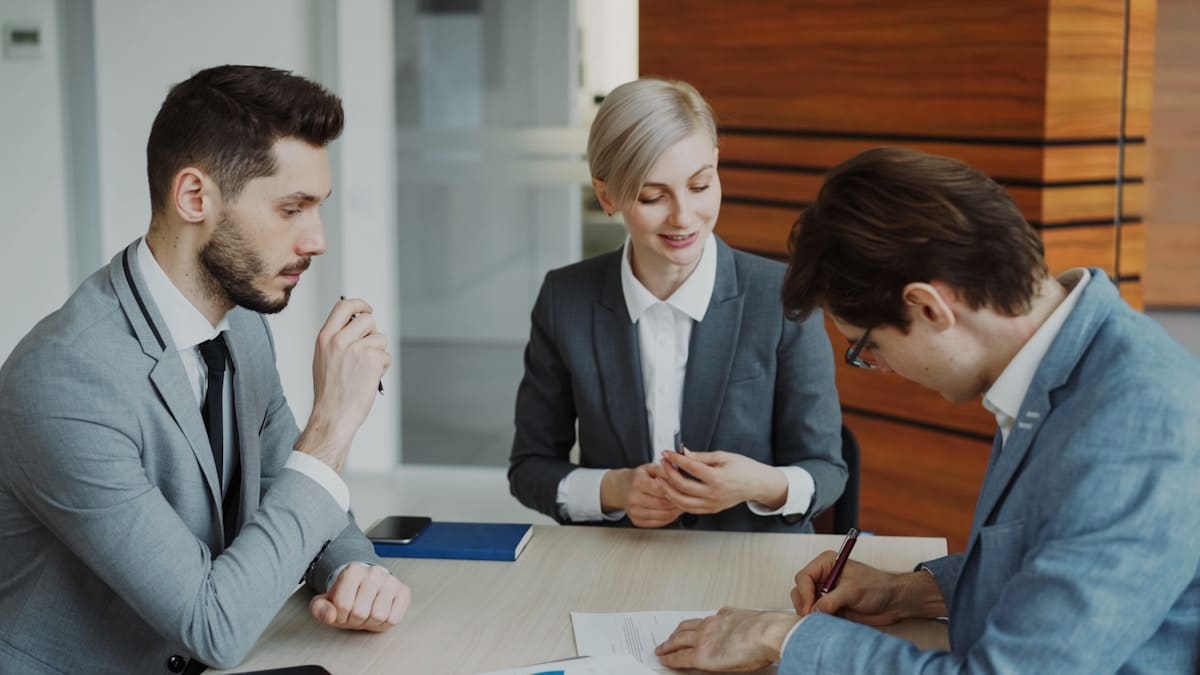 Trois professionnels en costume discutent et examinent des documents lors d'une réunion.