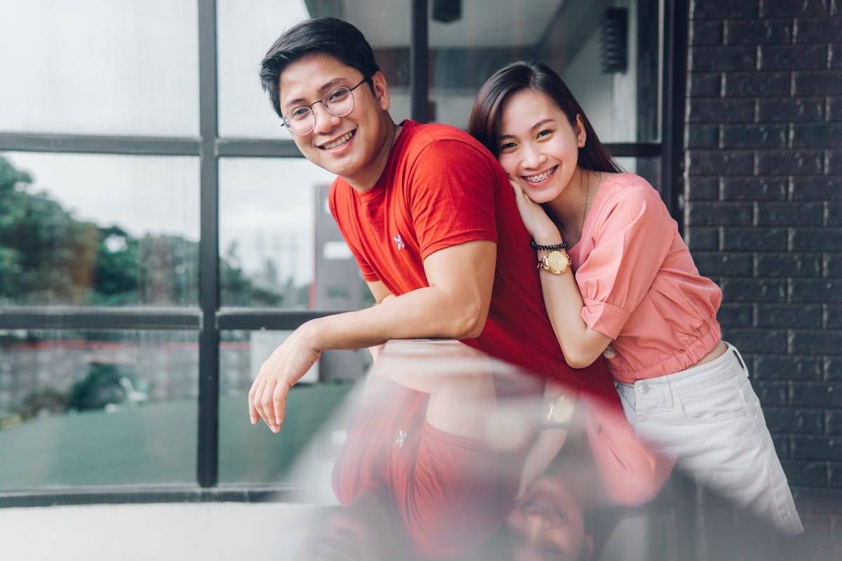Couple asiatique souriant devant une fenêtre.