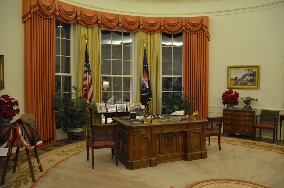 Bureau ovale décoré de rideaux dorés et de drapeaux américains.