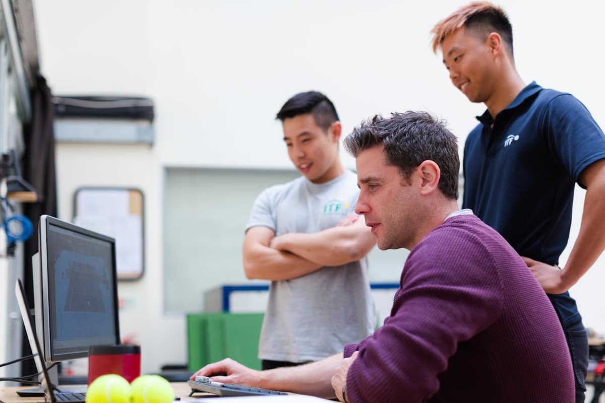 Trois jeunes hommes travaillant ensemble sur un ordinateur dans un espace de travail.