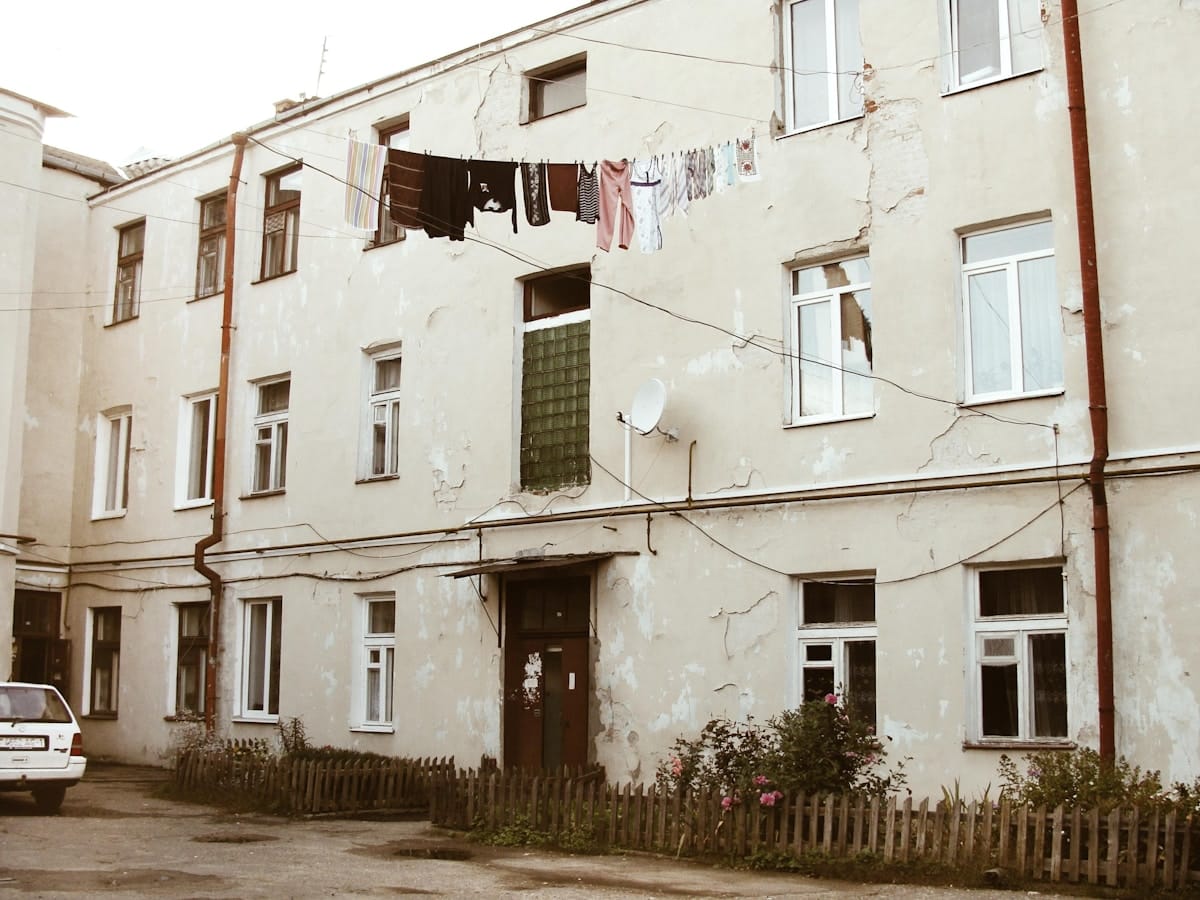 Bâtiment délabré avec linge suspendu, clôture en bois, fleurs sauvages.