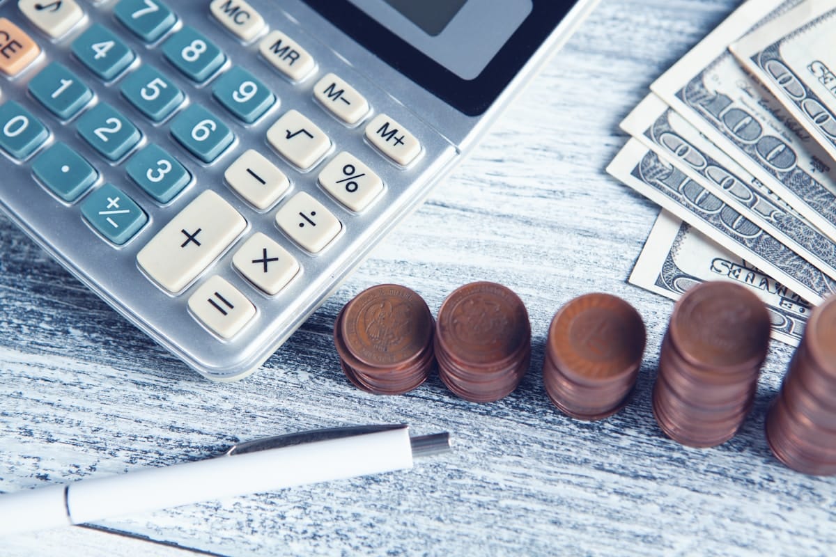 Calculatrice, pièces de monnaie, billets de banque, stylo, surface en bois.