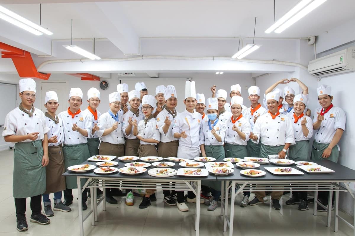 Groupe de chefs cuisiniers en uniforme blanc posant fièrement avec leurs plats.