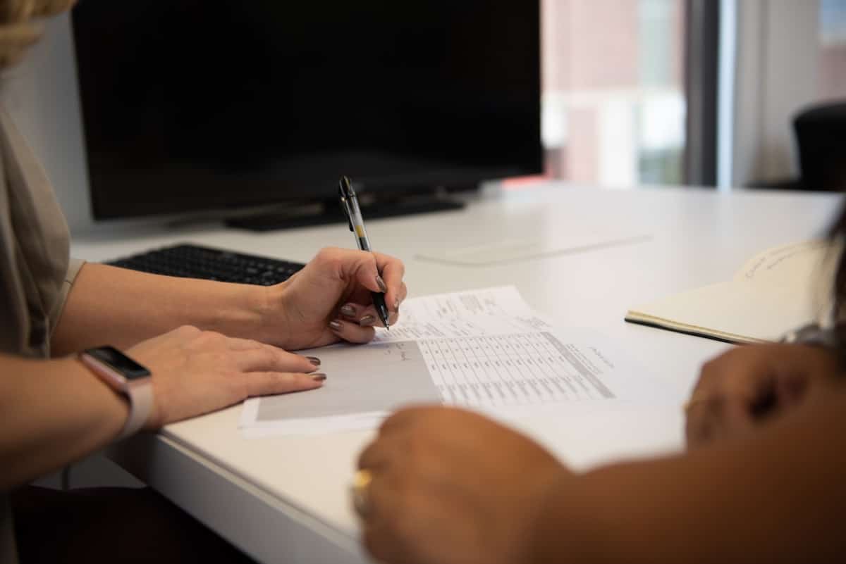 Personne écrivant sur des documents avec un ordinateur en arrière-plan.