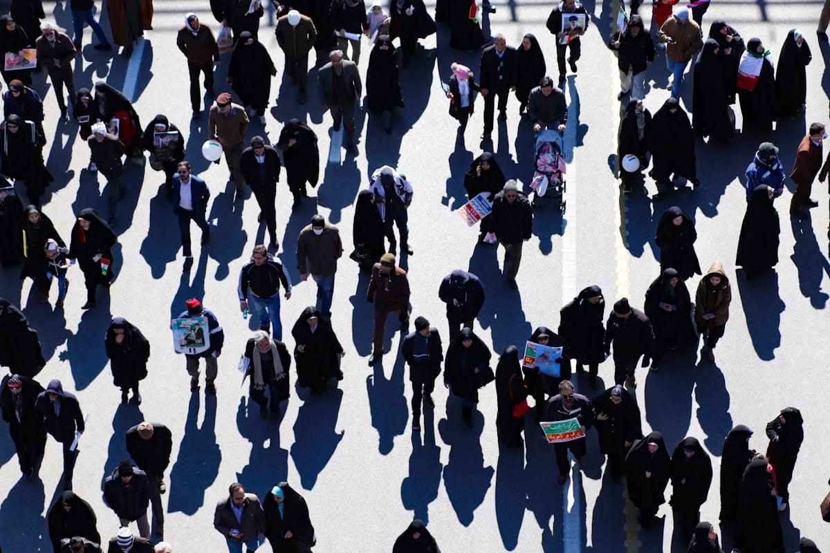 Foule dense de personnes marchant dans une rue ensoleillée.