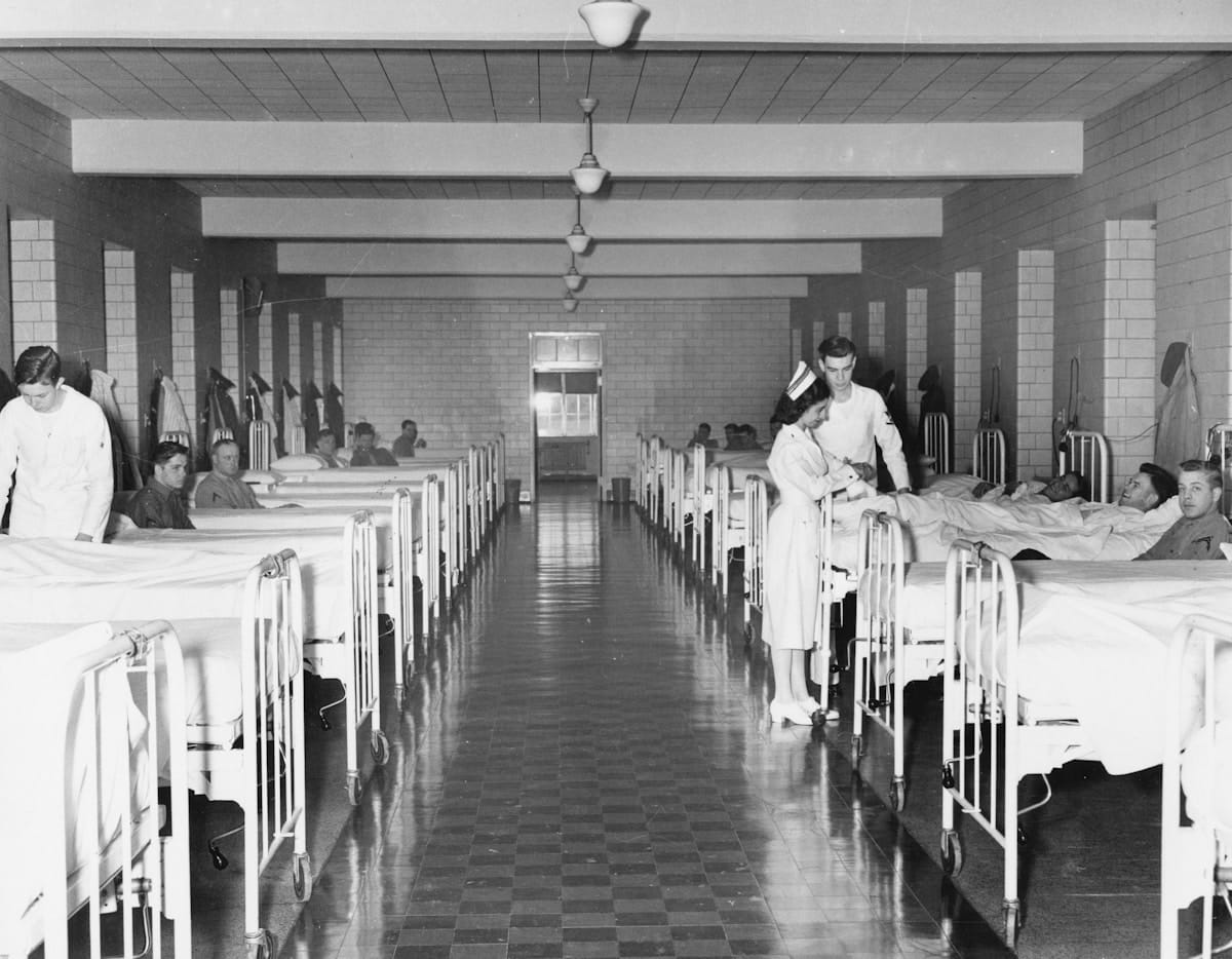 Salle d'hôpital avec des patients alités et du personnel médical.
