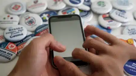 Militantisme social 2026 : main tenant un téléphone portable avec badges et boutons caritatifs pour une campagne en ligne.