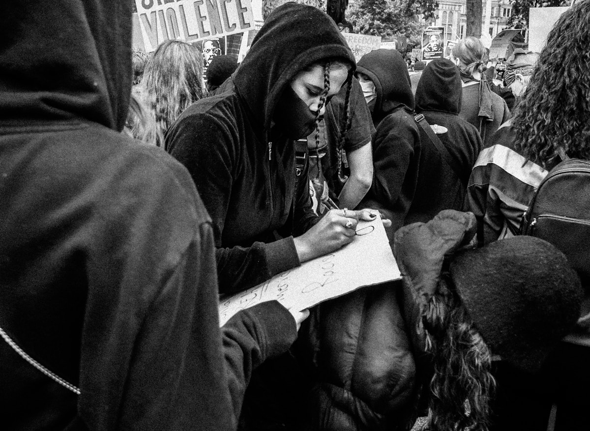 Manifestants encapuchonnés écrivant sur une pancarte lors d'une manifestation.