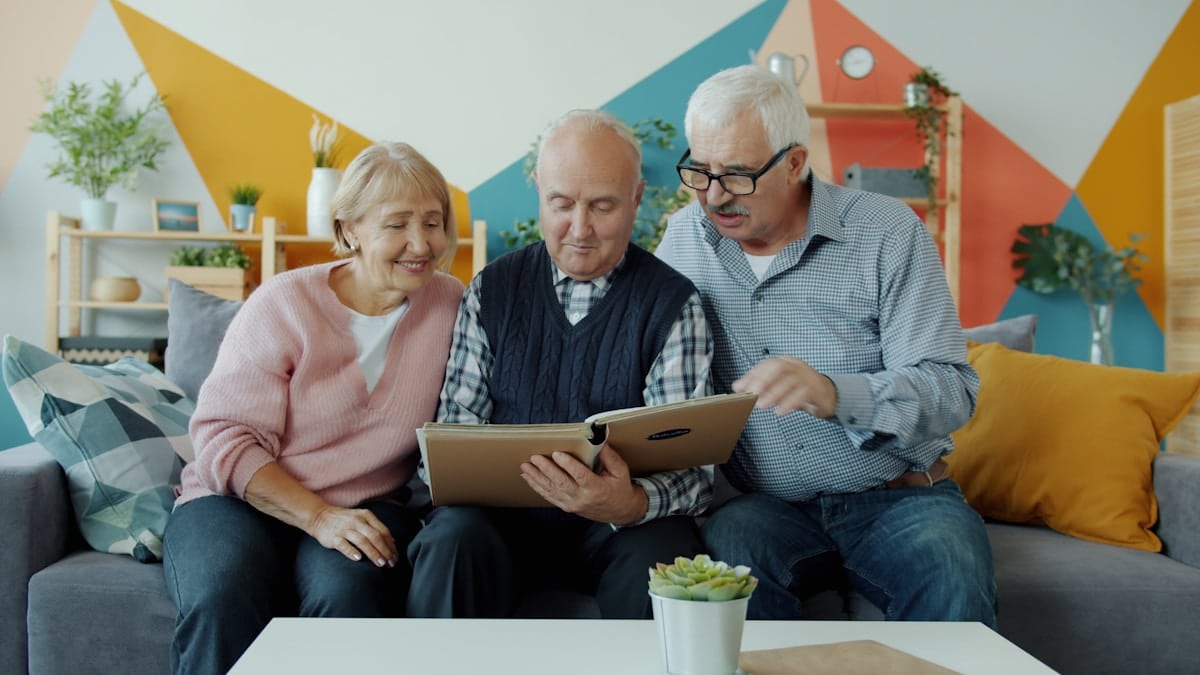 Trois personnes âgées assises sur un canapé, utilisant une tablette numérique ensemble.