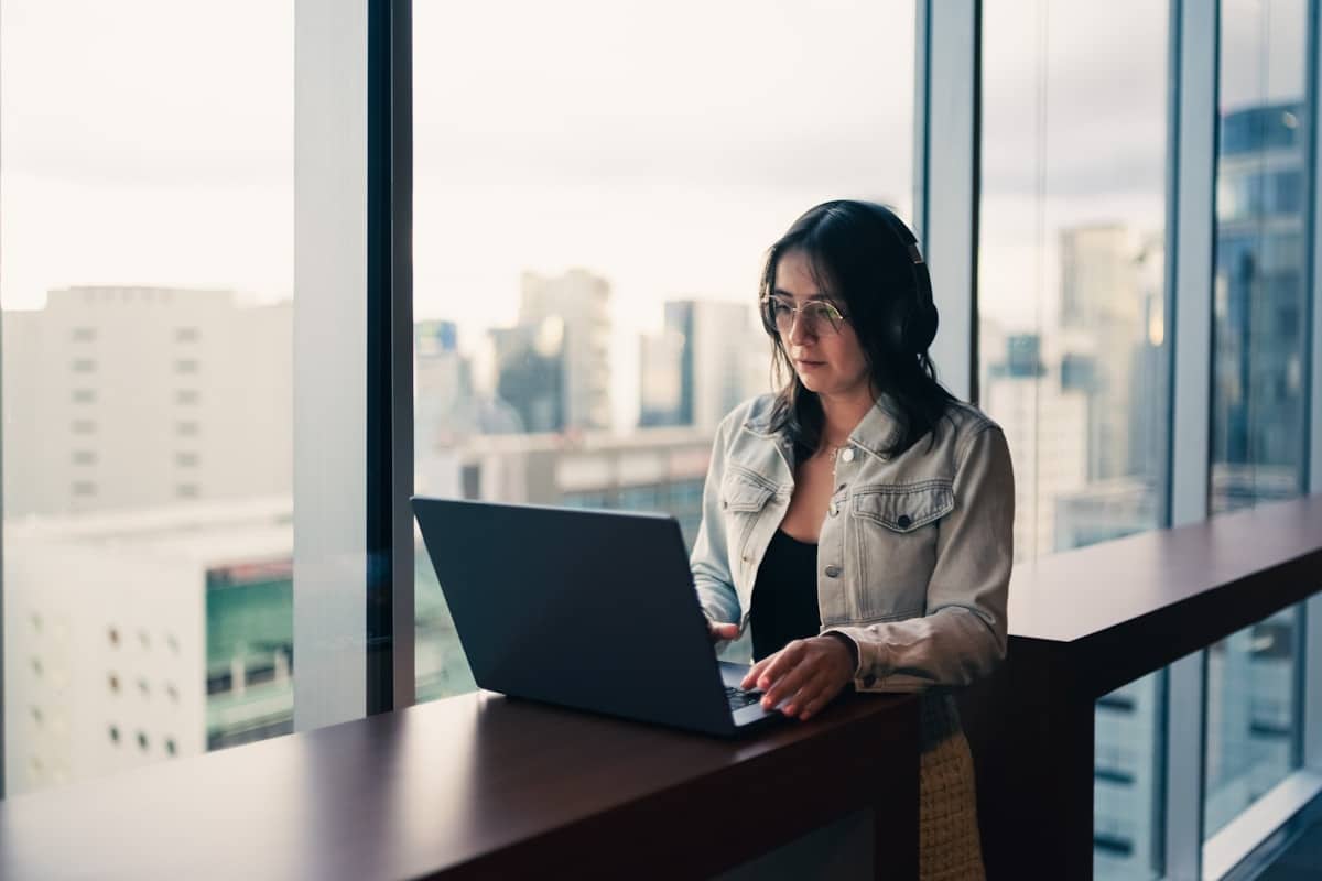 Femme assise devant un ordinateur portable, regardant par la fenêtre.